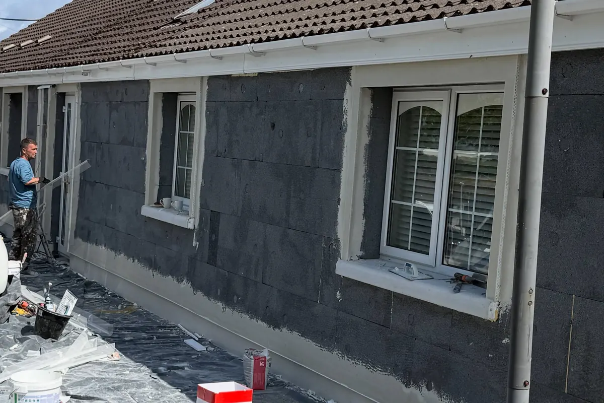 Grey insulation boards fixed across the front of a bungalow, materials stacked on the drive